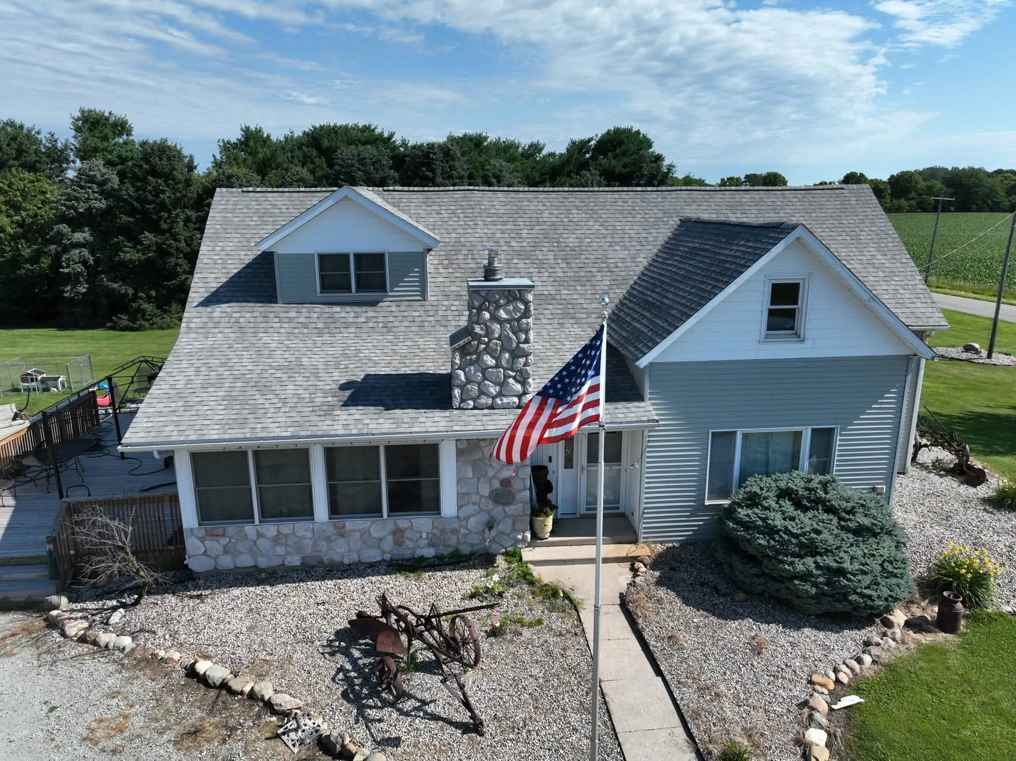 The finished farmhouse from the front, with its new light gray shingle roof, stone chimney and dormer