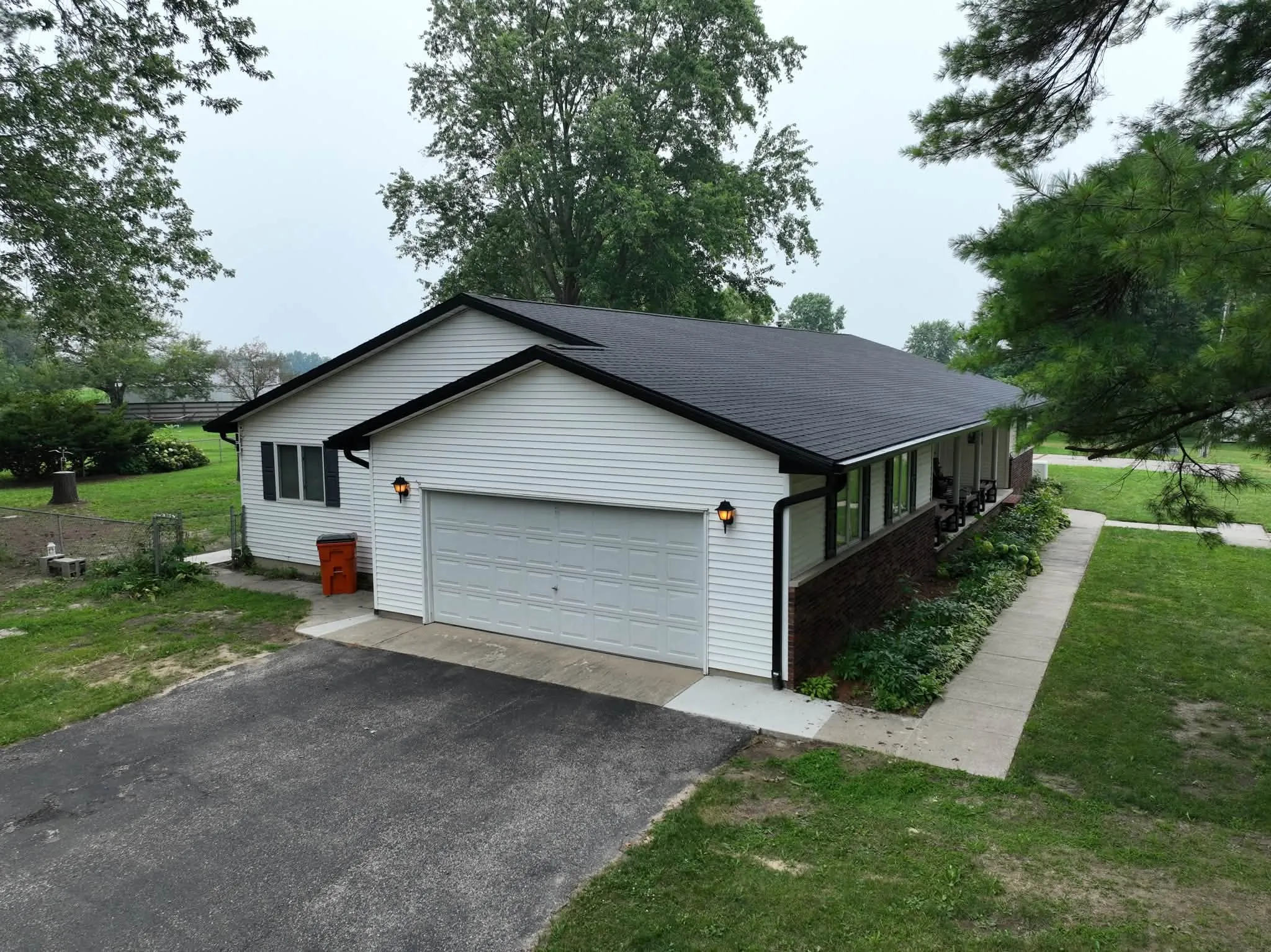 The garage end of the house from the air, showing the new black roof, fascia, and downspout against white siding