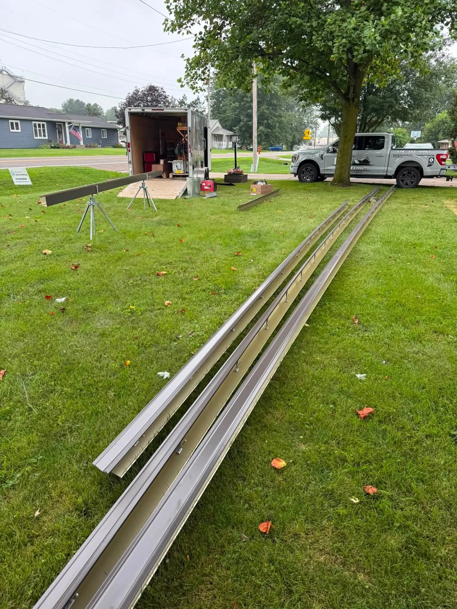 Long runs of freshly formed seamless gutter laid out on the lawn beside the trailer they were rolled from