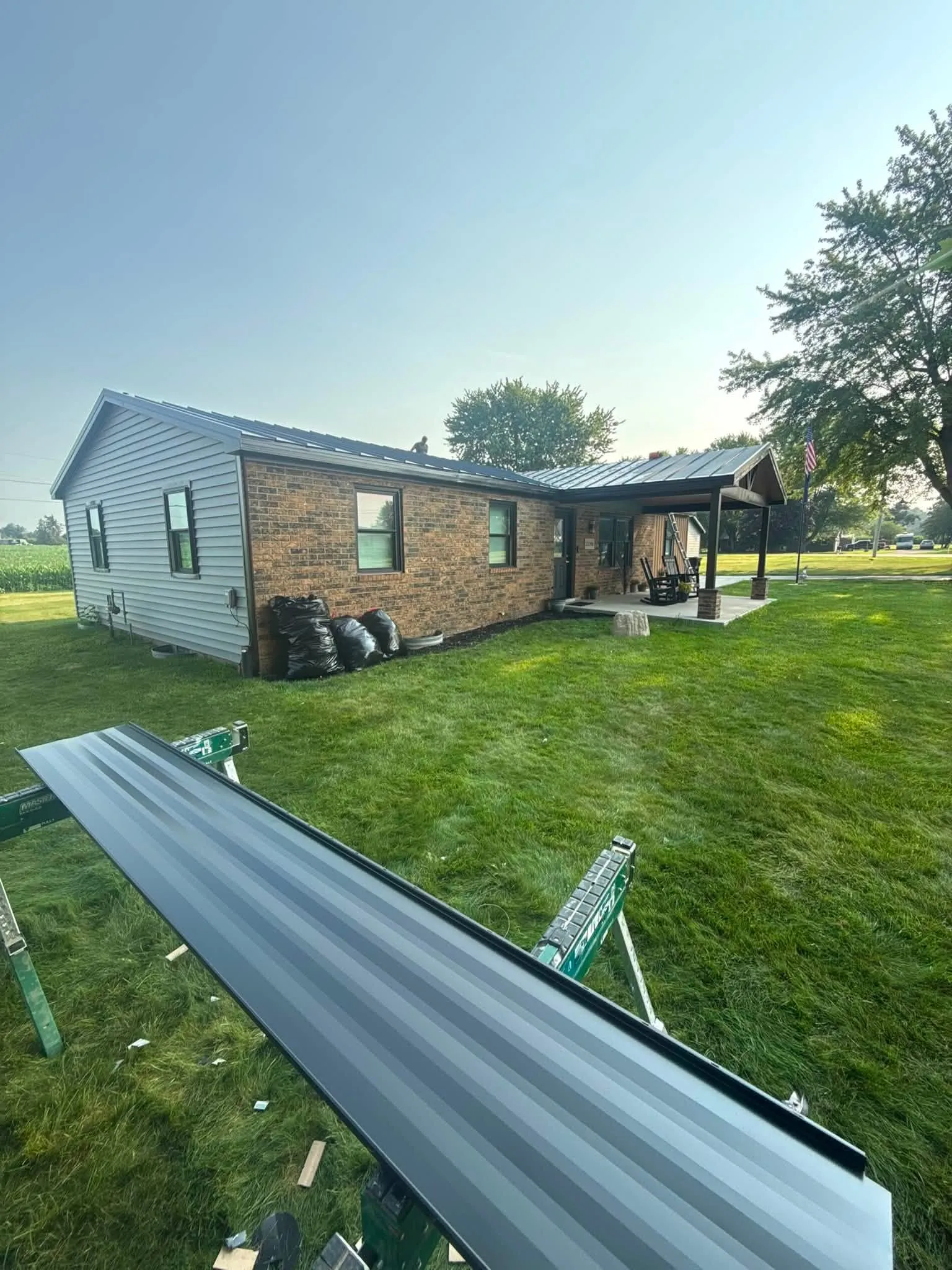 A full-length panel resting on sawhorses in the yard, with the part-finished roof on the brick ranch behind