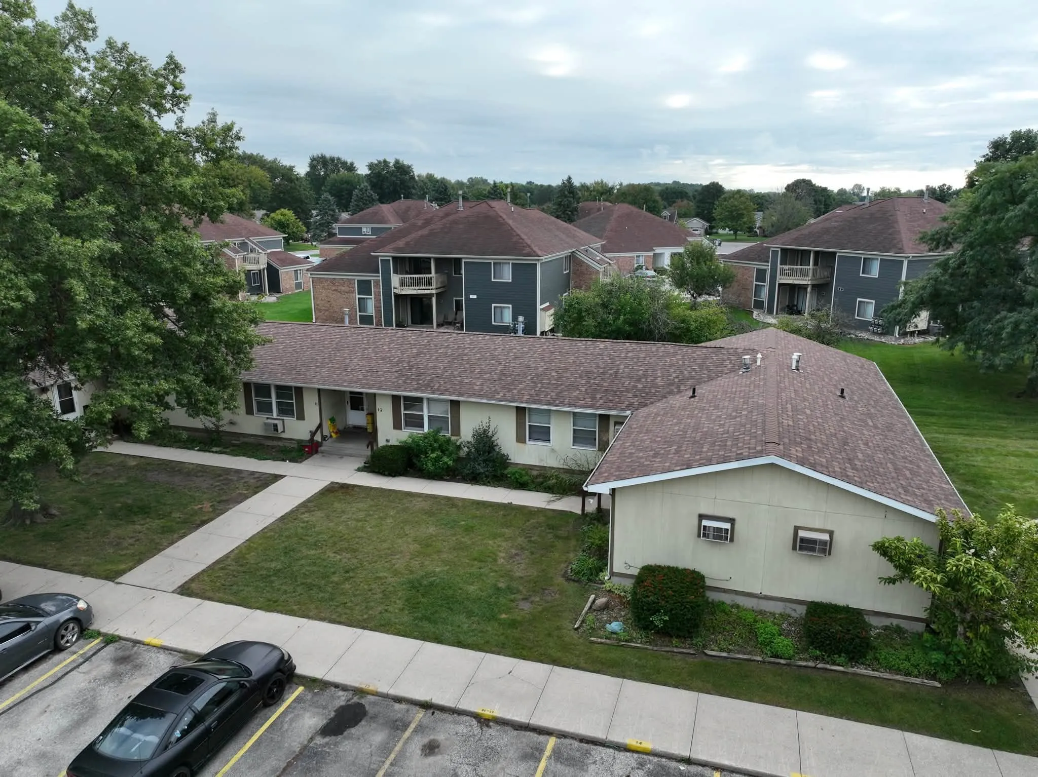 One of the single-story apartment buildings under its new Desert Rose shingle roof, with the parking lot in front and two-story buildings behind