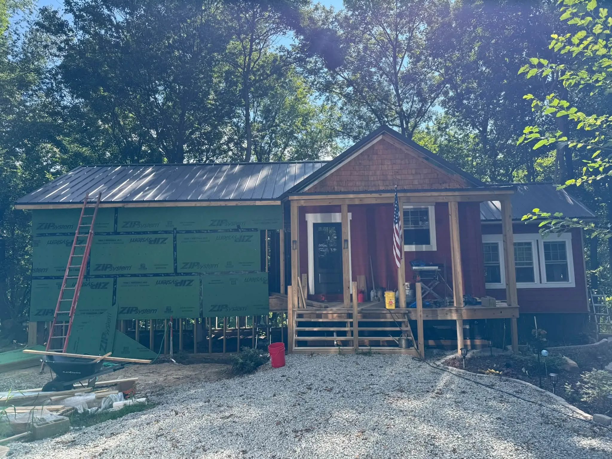 The cabin in the woods with its new Dark Bronze metal roof, a front porch on wood posts, and housewrap still on one side
