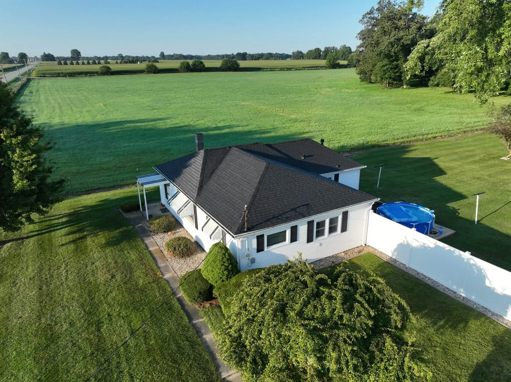 The white home with its new black hip roof, black shutters, and fields stretching out behind it