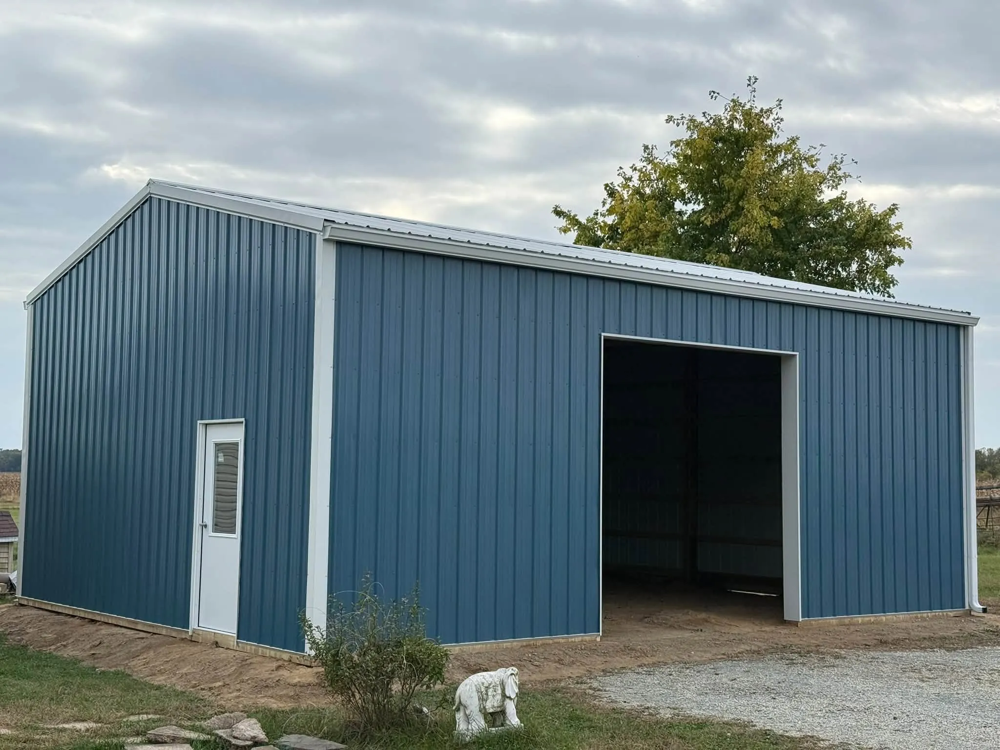 The finished pole barn garage in blue steel with white trim, a white walk door on the side and a wide open bay at the front