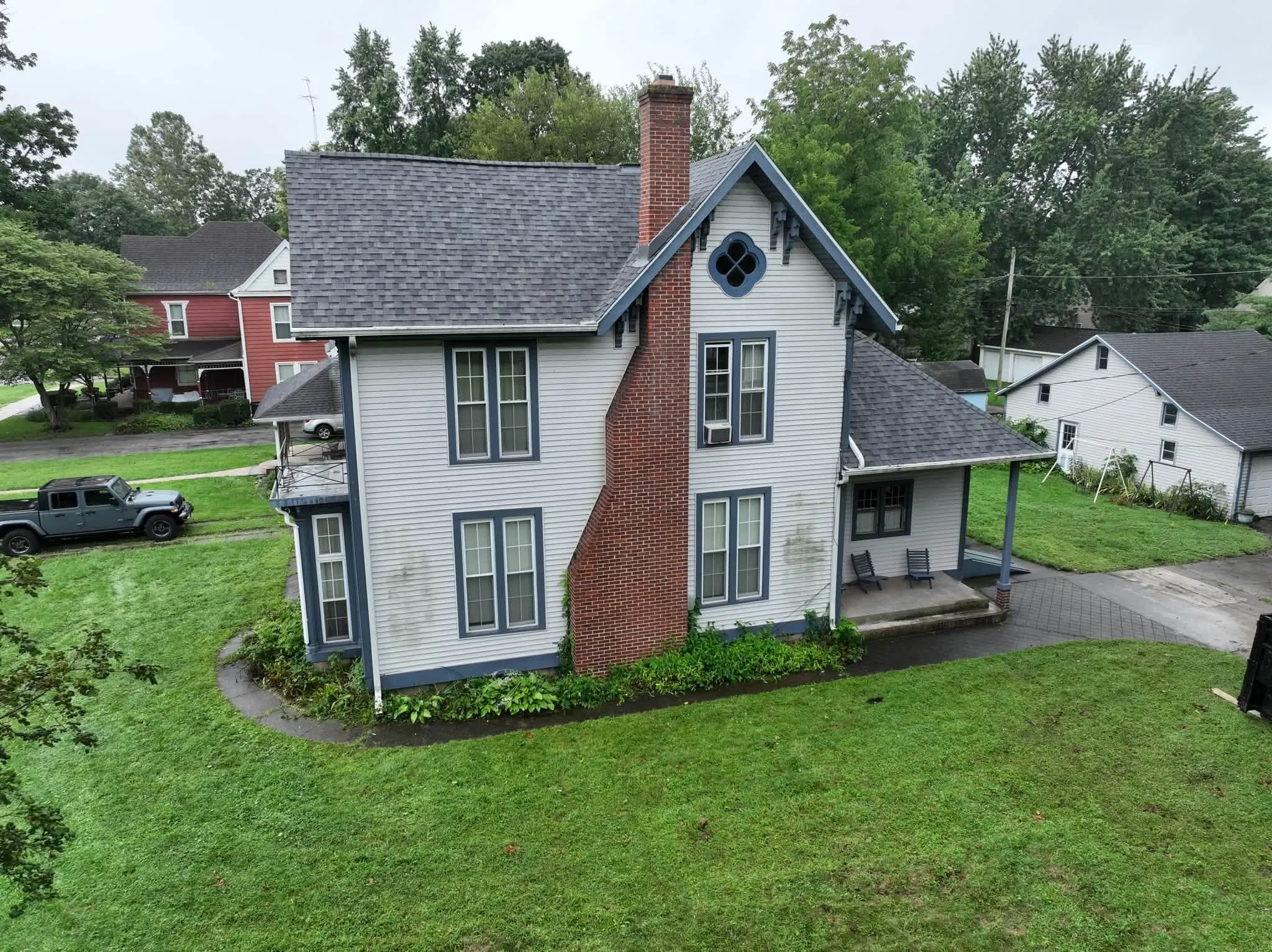 The two-story home with its new Estate Gray roof, a tall brick chimney up the side, and the round window in the gable