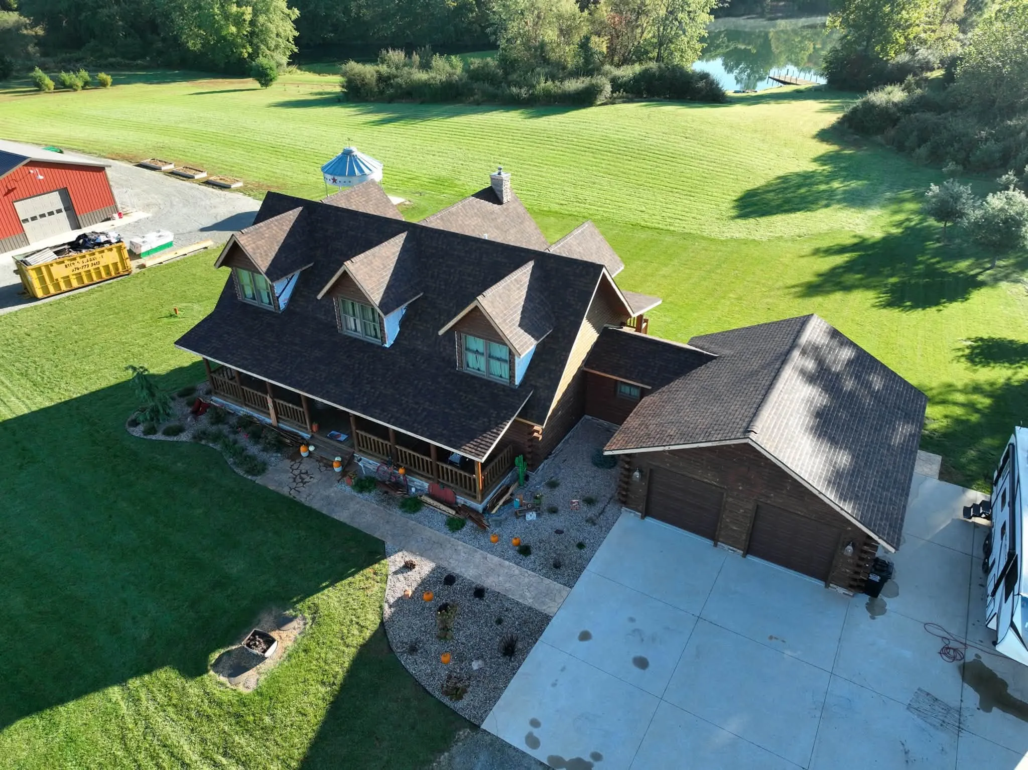 The log home under its new Burnt Sienna roof, with three dormers over the wraparound porch and the garage alongside