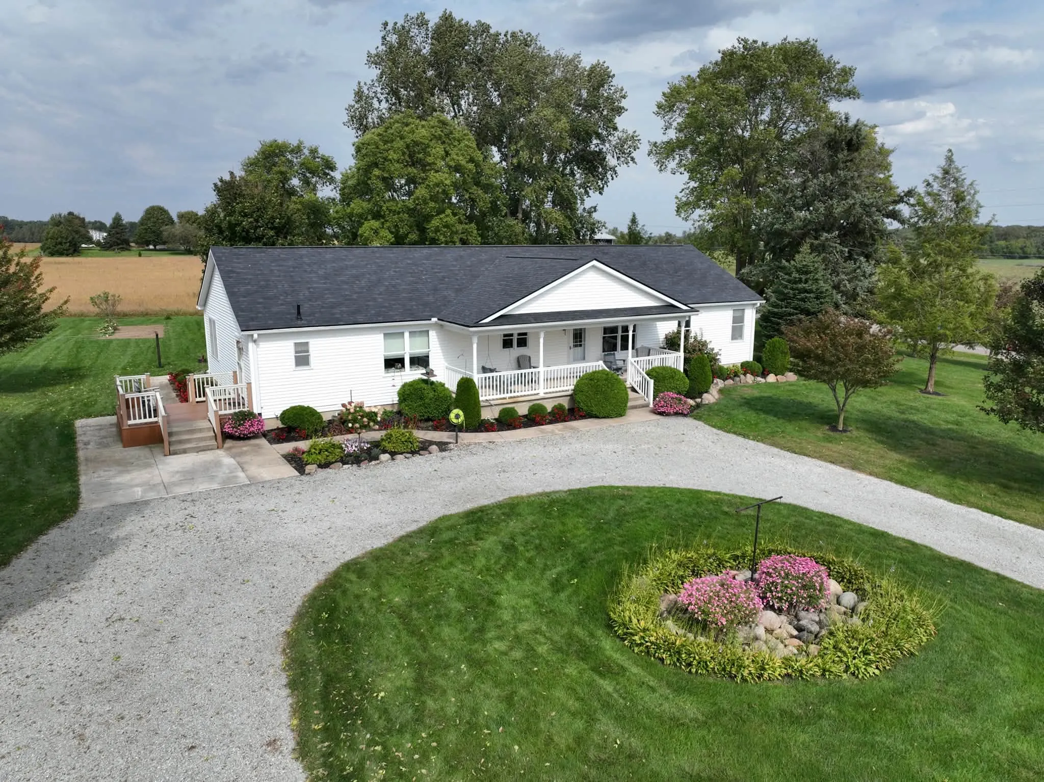 The white ranch home under its new Onyx Black roof, with the covered front porch and the flower bed in the middle of the circle drive