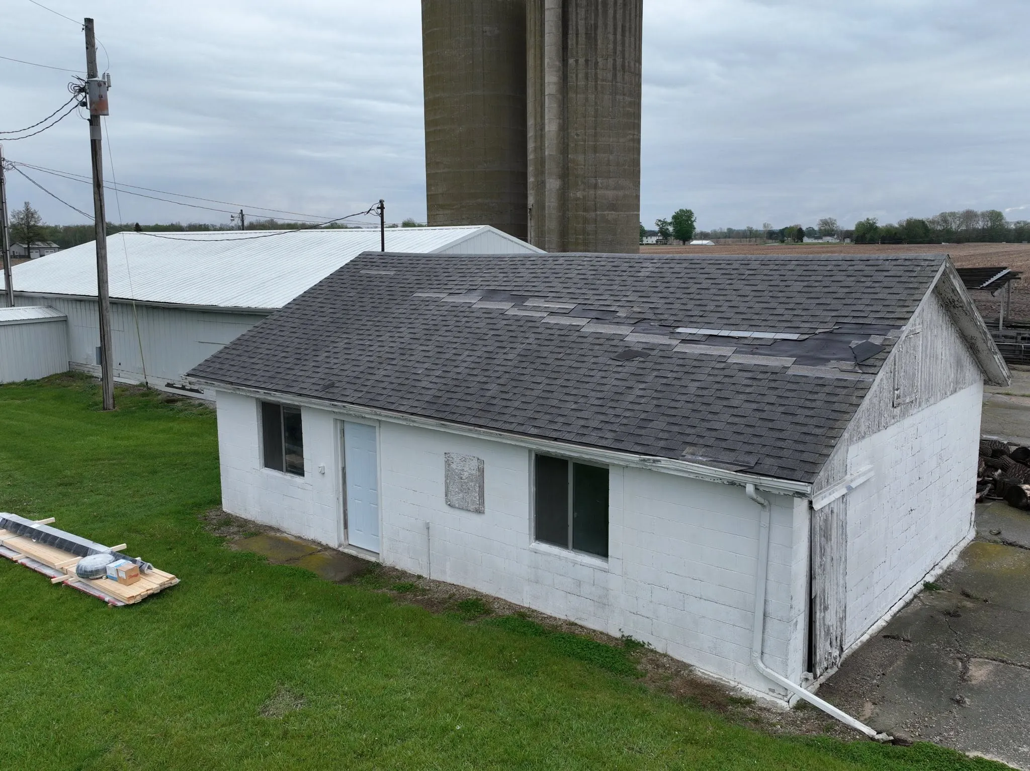 Worn shingle roof on a white block barn outside Rochester, with new metal panels staged on the lawn