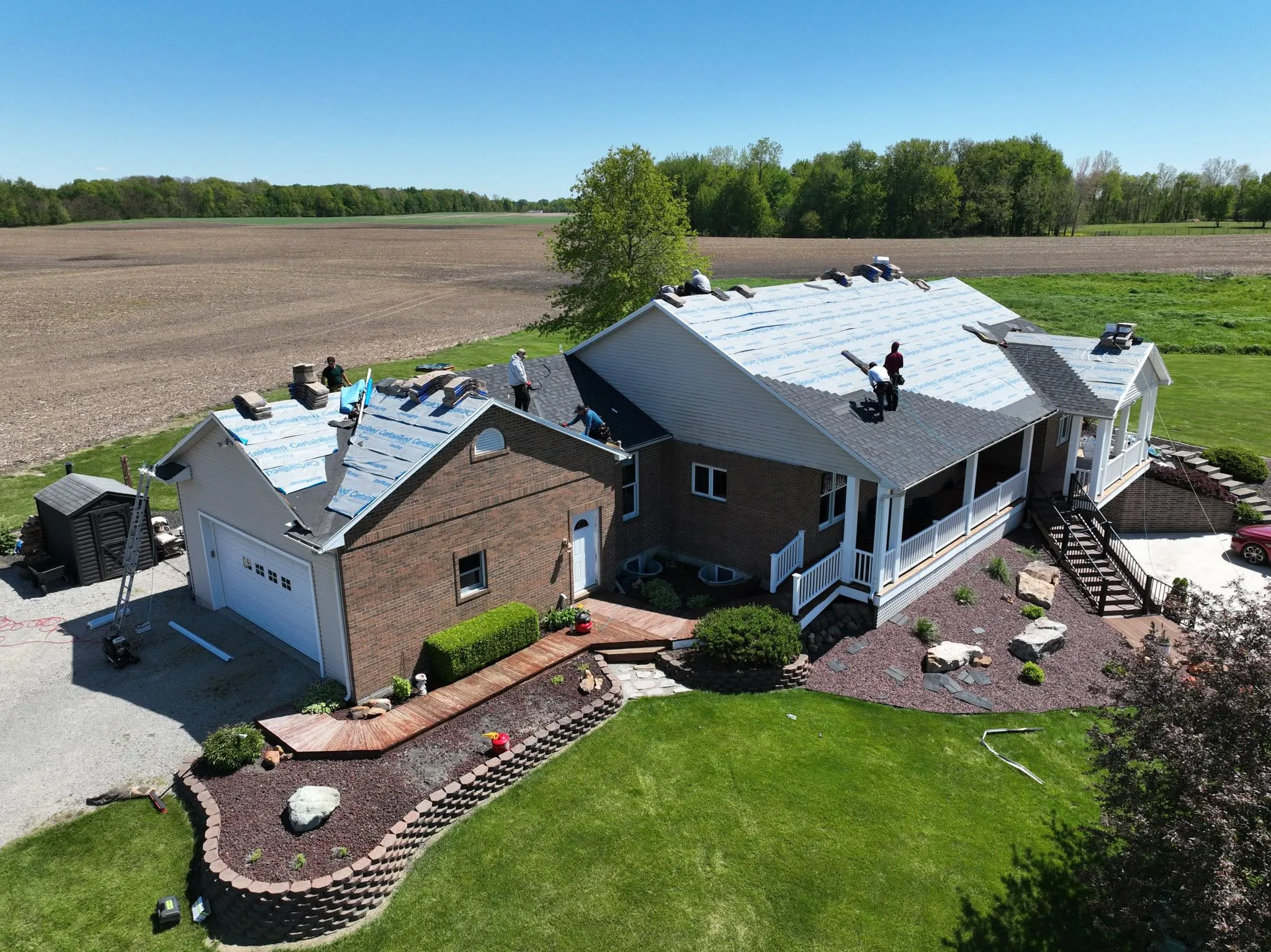 The crew part way through the install, with CertainTeed underlayment down across the deck and shingle bundles staged along the ridge