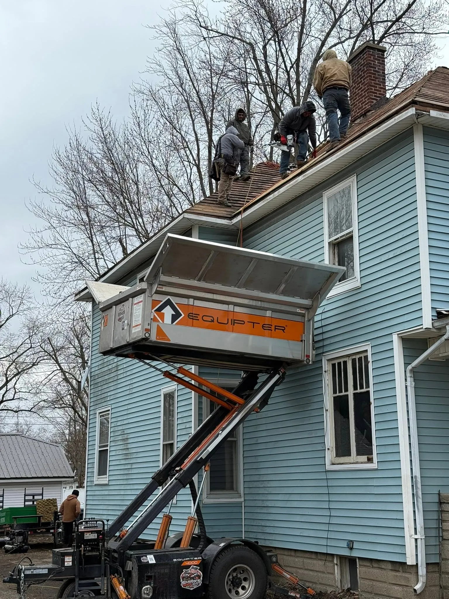 The crew tearing off at the eave with a lift trailer raised alongside to catch the old material