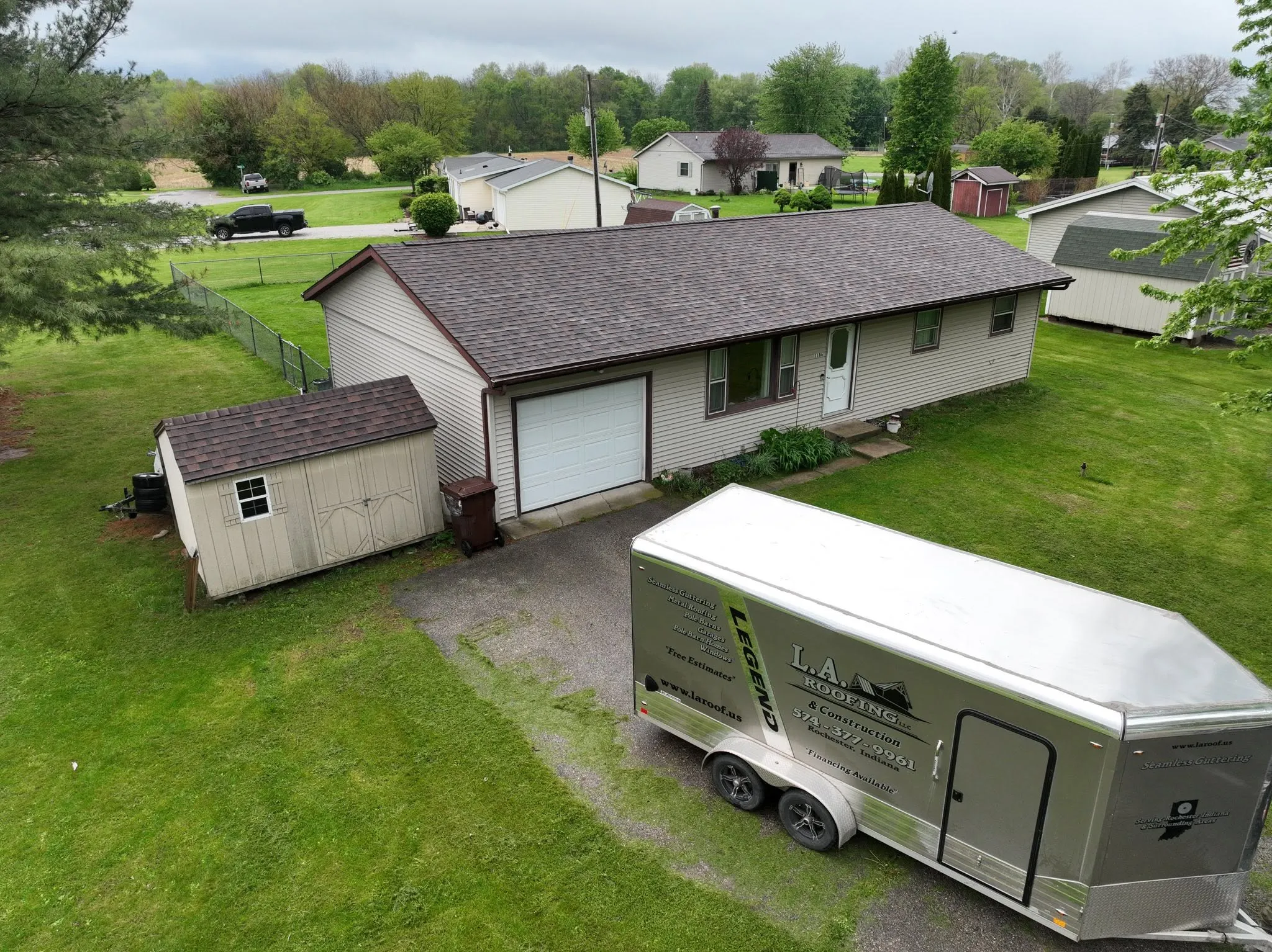 The finished ranch from the air with its new Brownwood roof, the matching shed alongside and the L.A. Roofing trailer in the drive