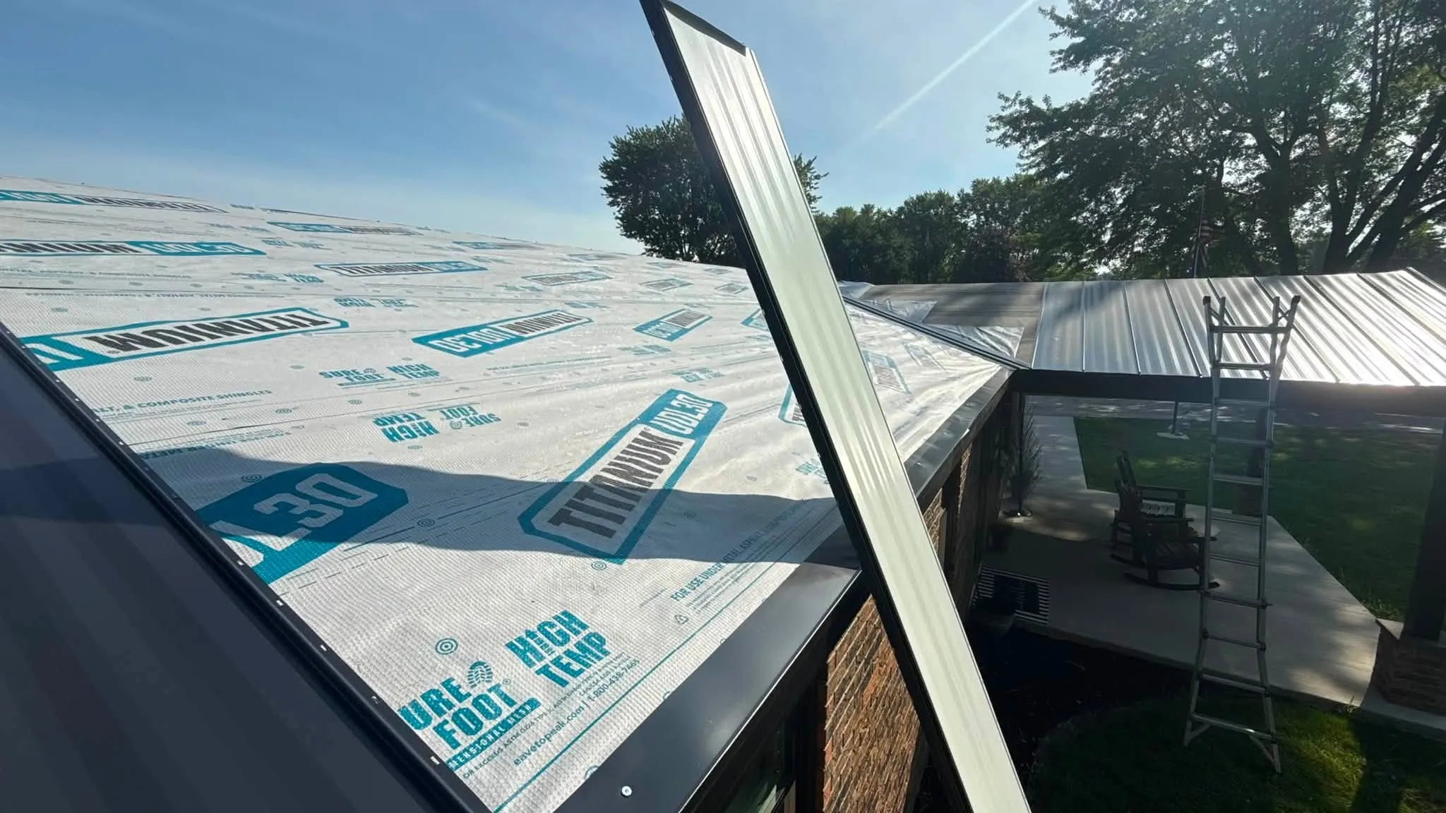 High-temp synthetic underlayment down across the deck, with a standing seam panel being lifted into place