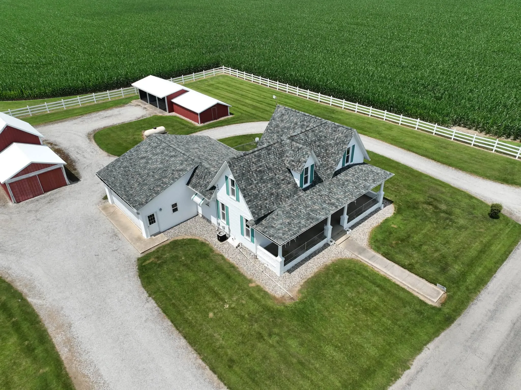 The farmhouse and its porch from the other side, with the cornfield and white fence beyond