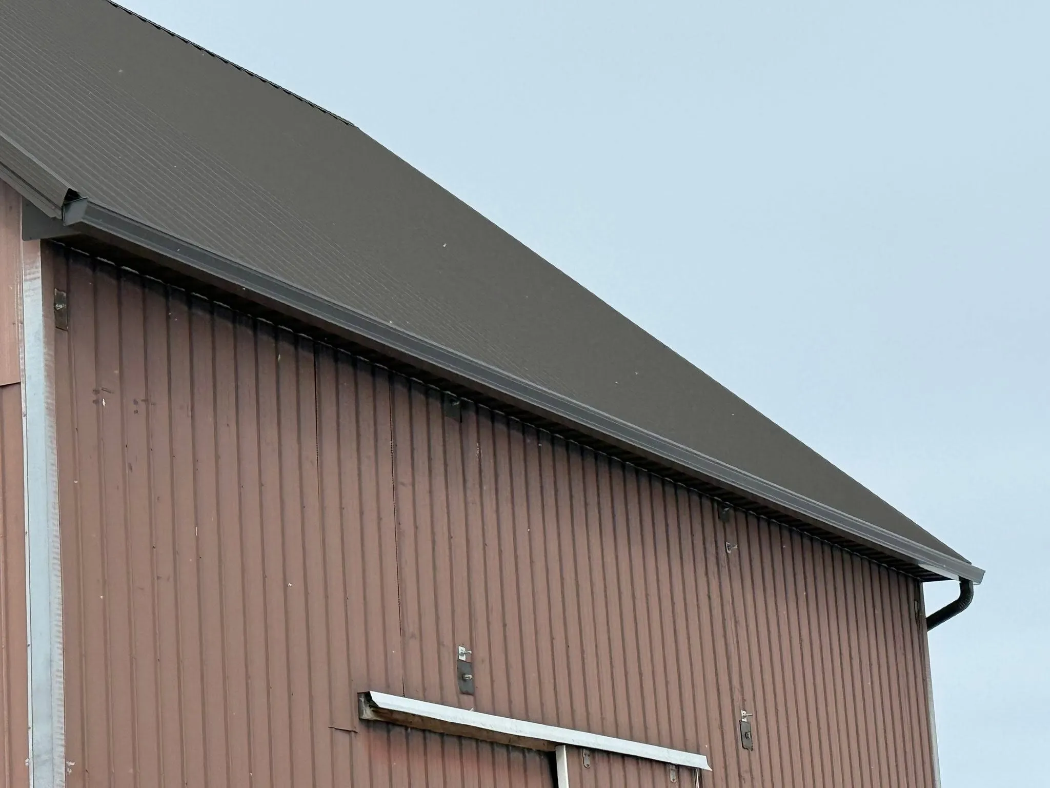 The finished soffit, fascia, and gutter running the length of the barn eave, with the downspout at the far corner