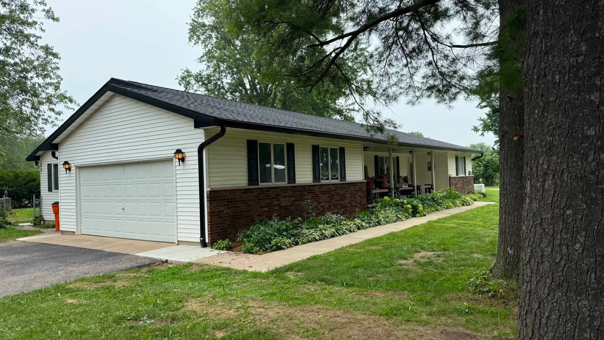 The front of the house from the driveway, with the black roofline above the white siding and brick