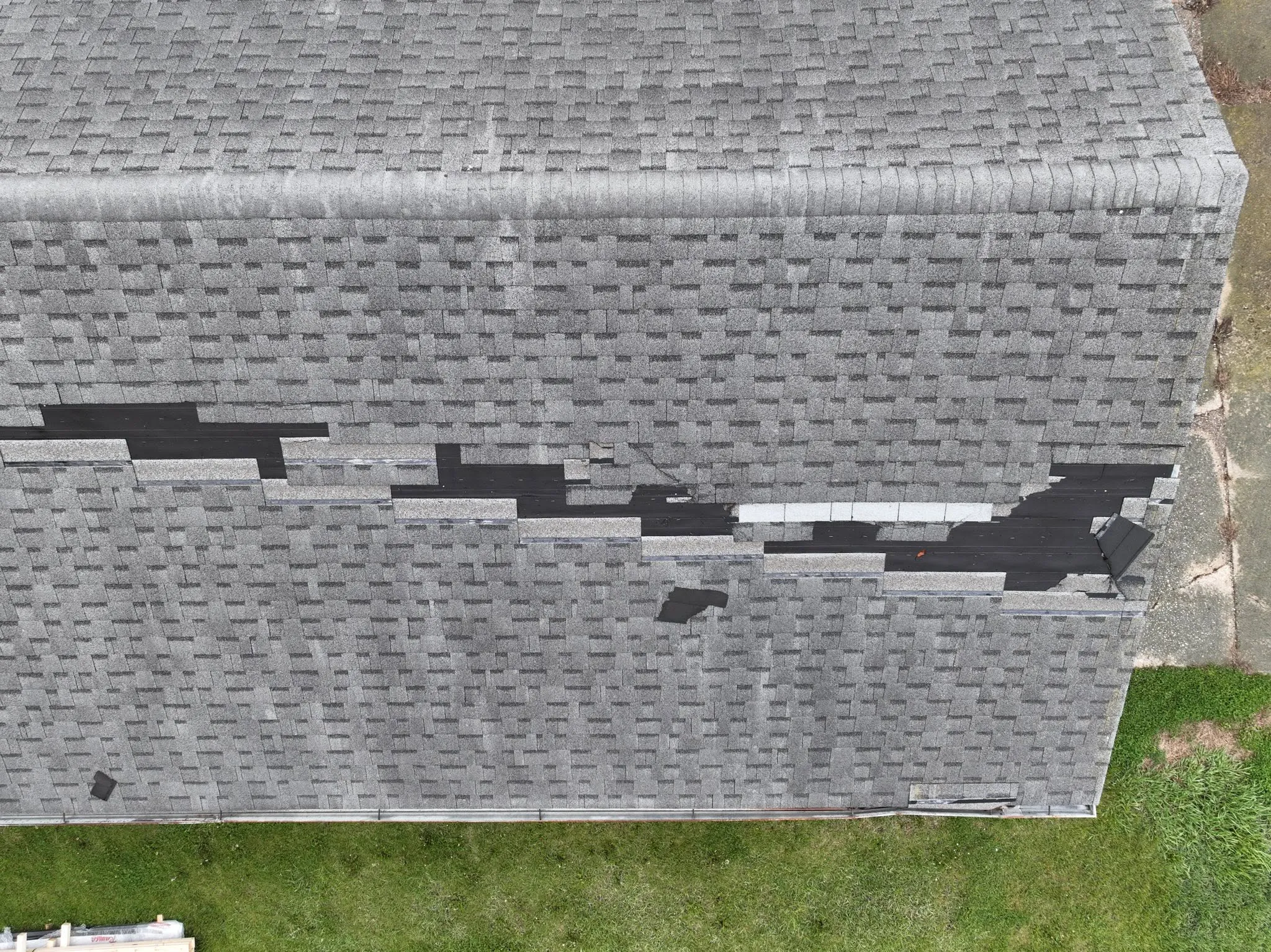 Overhead view of the old roof showing rows of missing shingles and exposed underlayment
