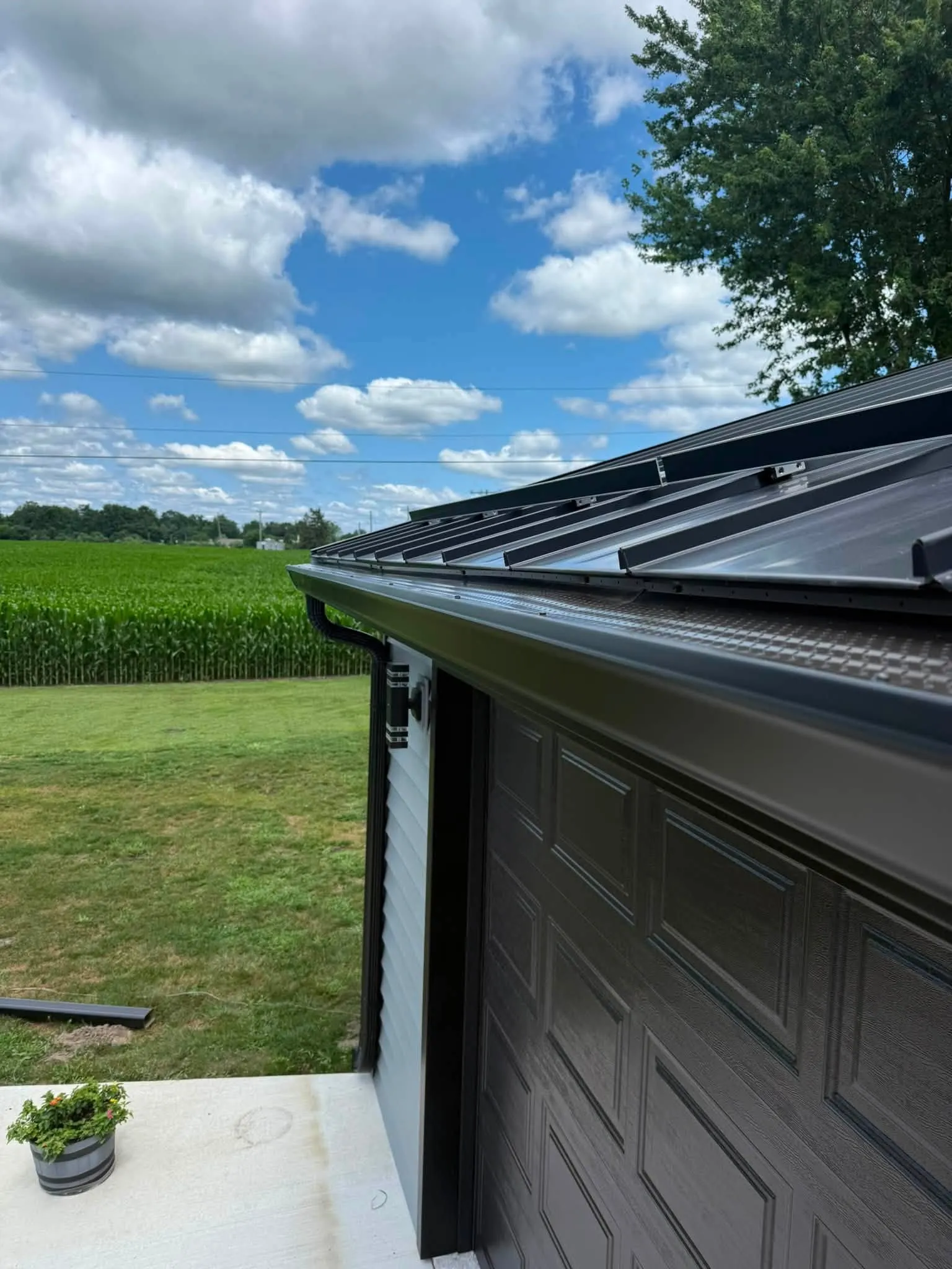 The gutter run above the garage door, with the downspout turning down at the corner and a cornfield beyond