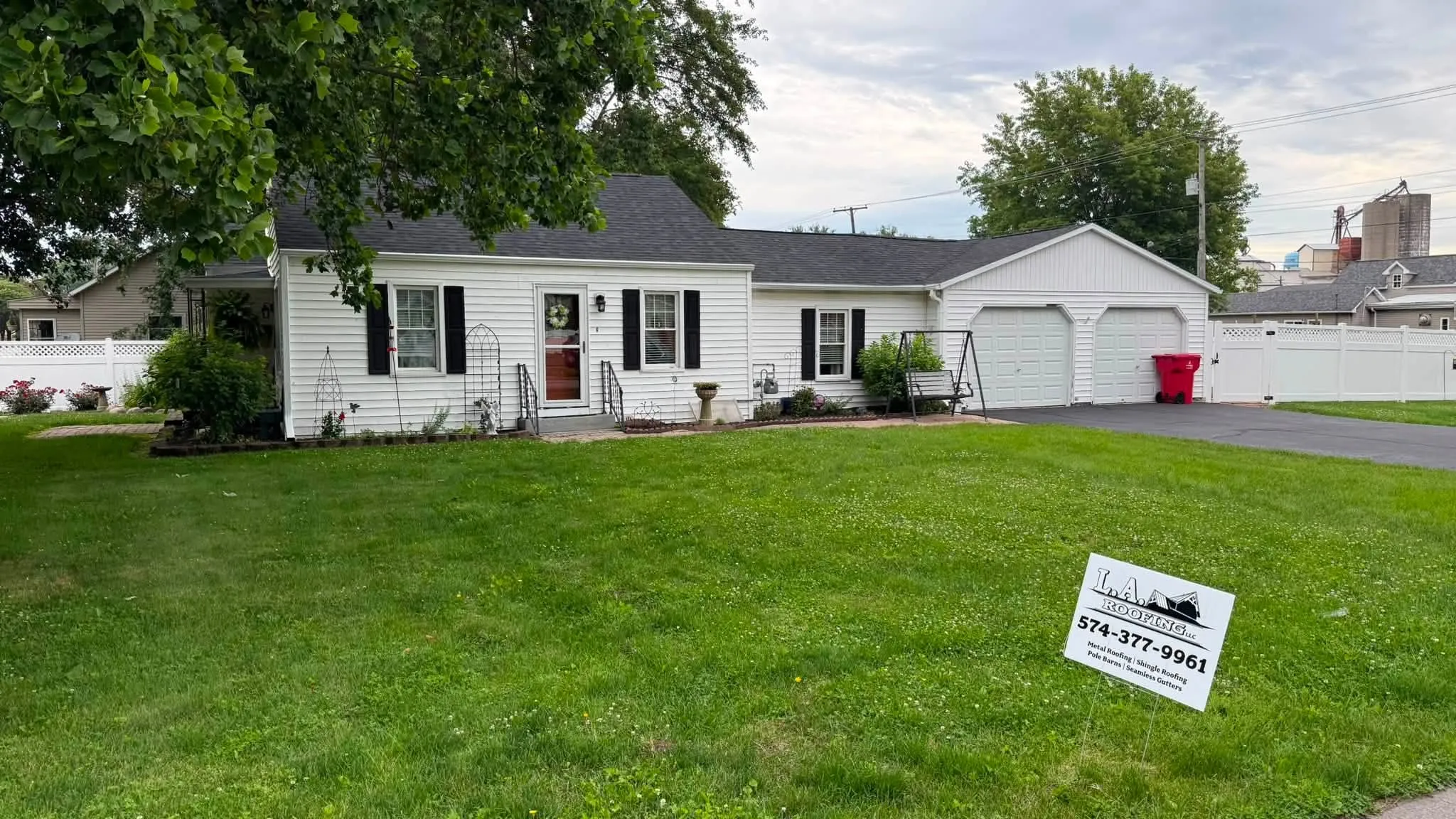 The house from the side with an L.A. Roofing sign in the yard and the grain elevator in the distance