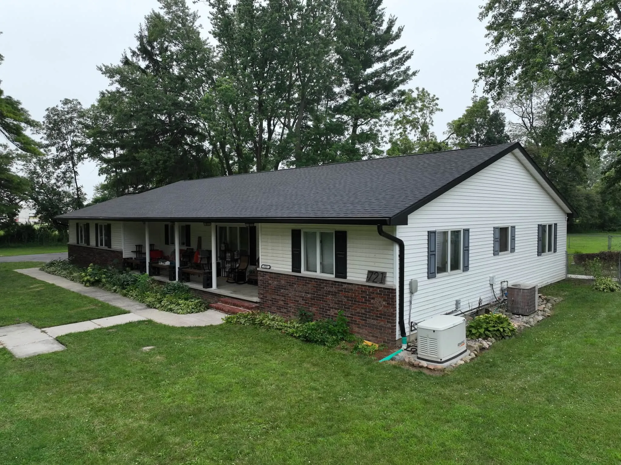 The finished Winamac home from the yard, with the new black roof and black gutters running the length of the covered porch
