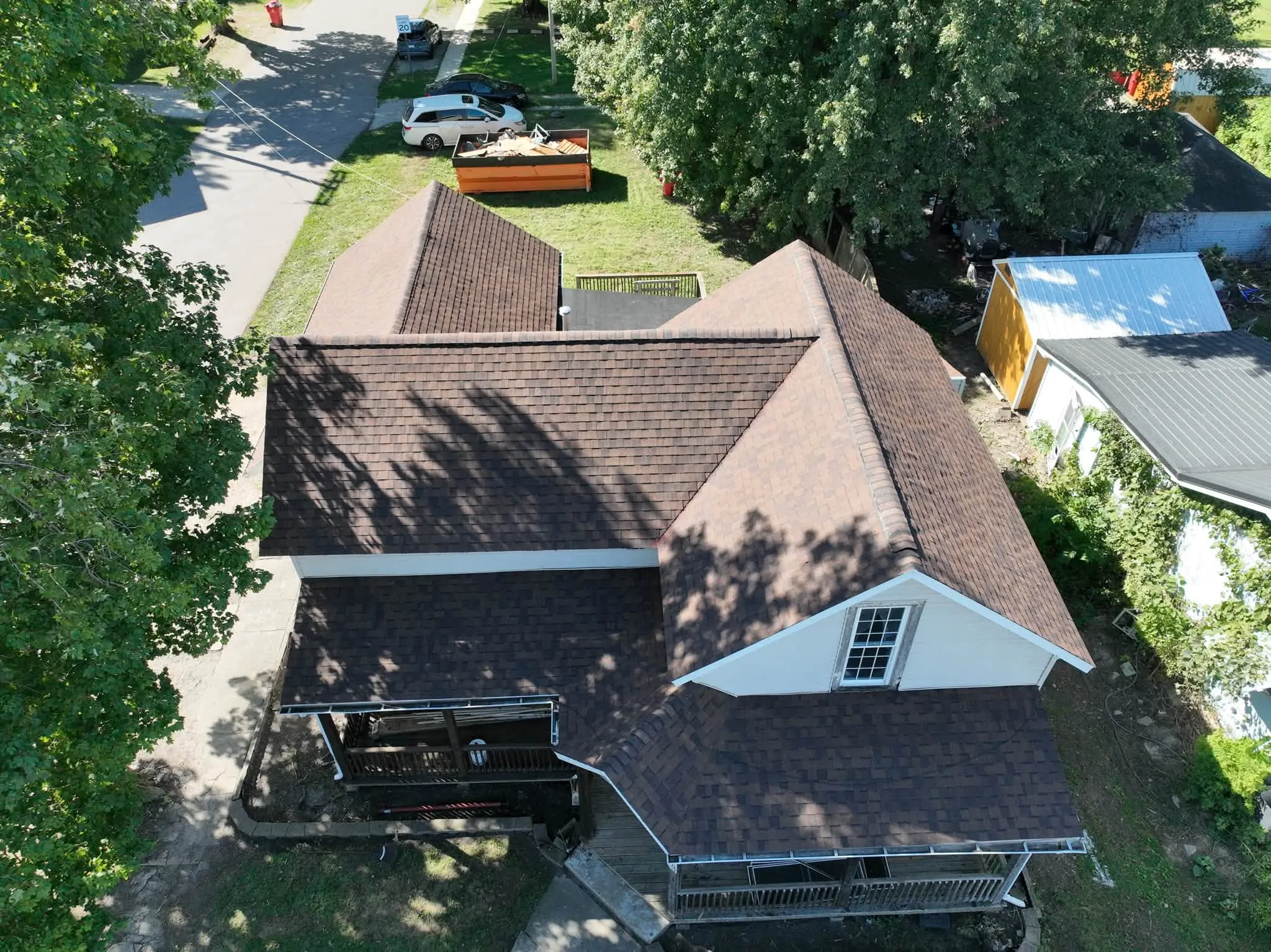 Higher view of the new roof, with the dumpster and a work trailer parked behind the house