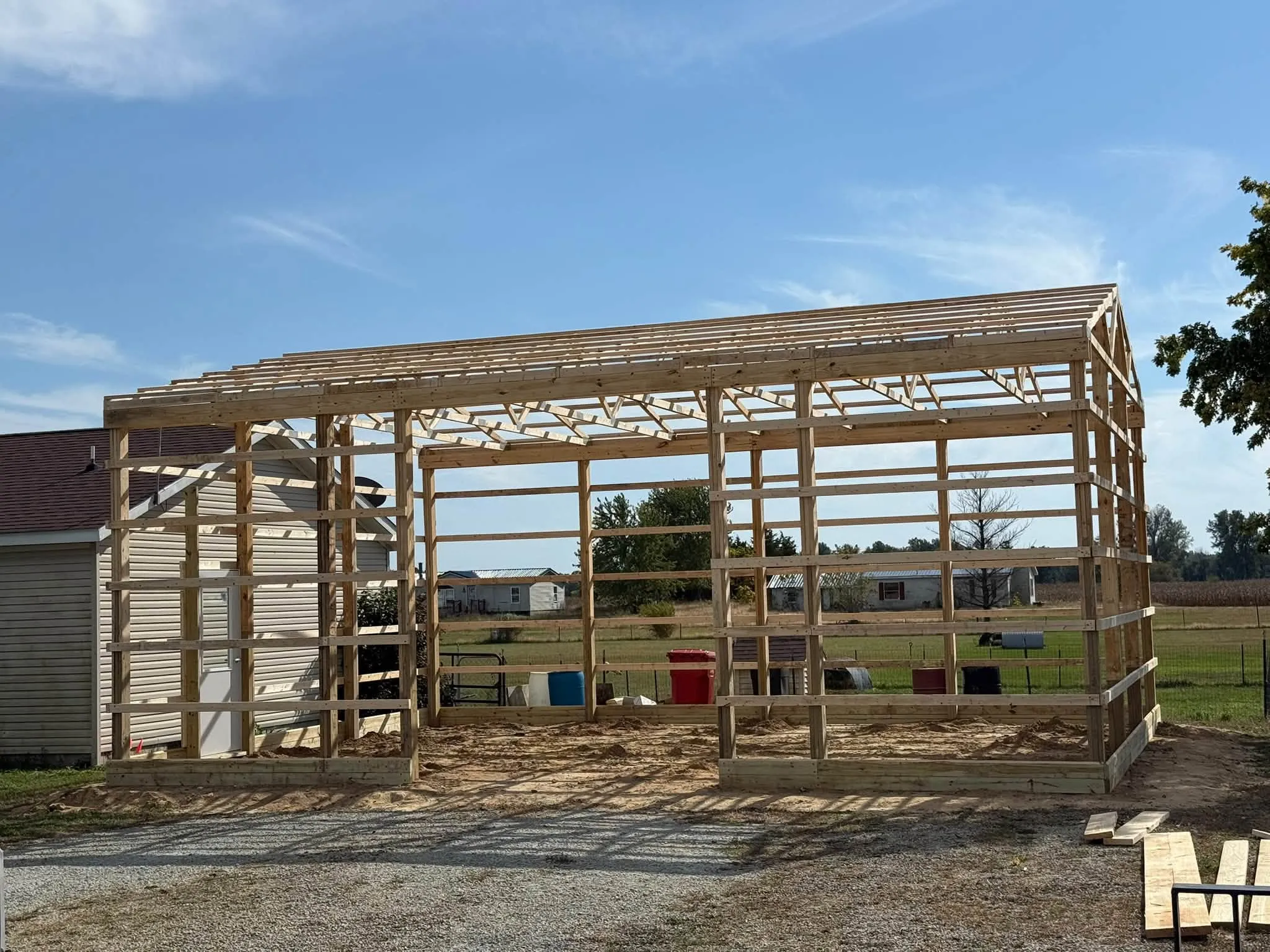 The bare wood frame standing on the gravel pad, with the trusses set across the posts