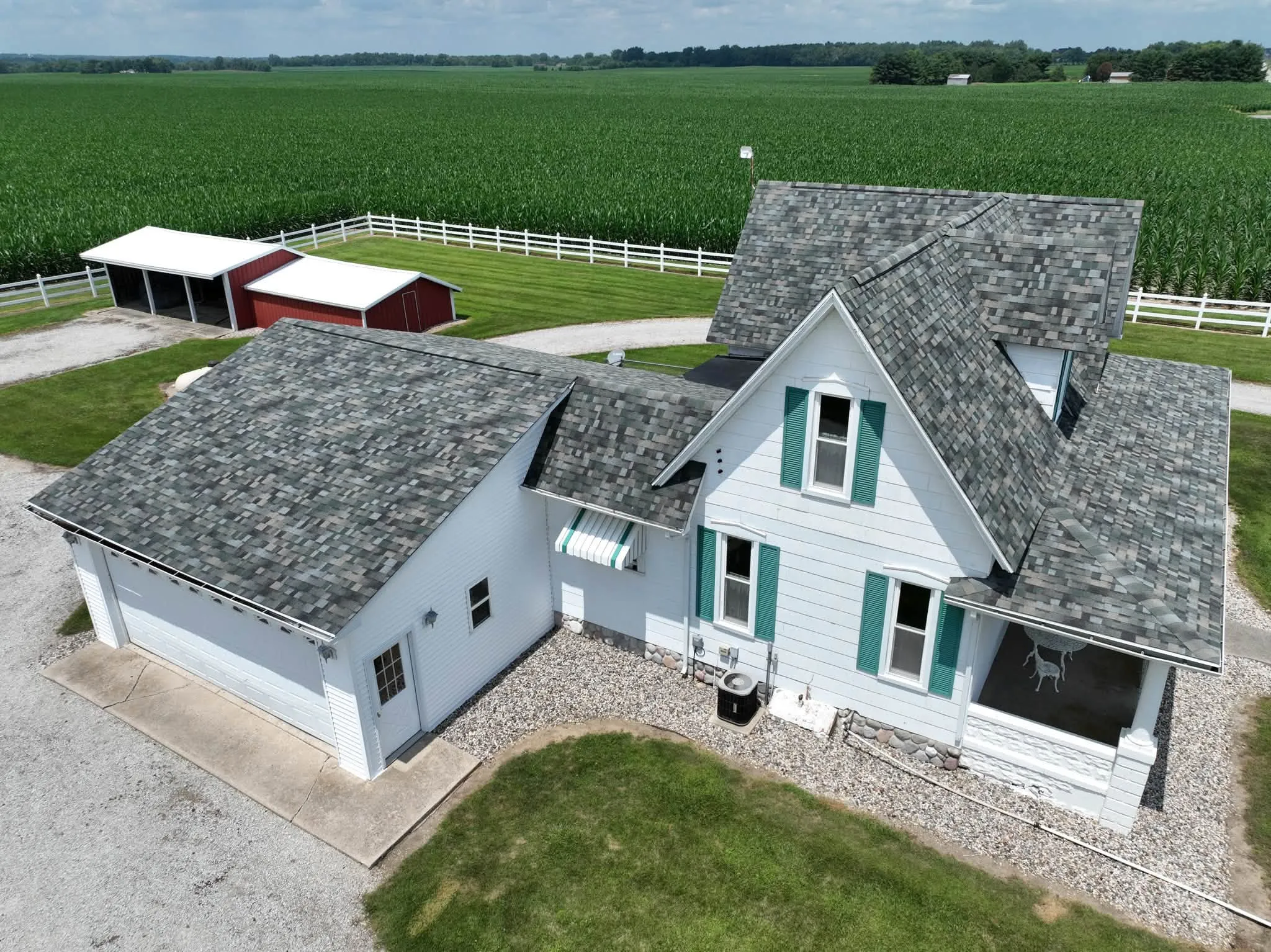 Closer aerial of the new roof, showing the green and gray blend of the Evergreen Mist shingles across the house and the garage wing
