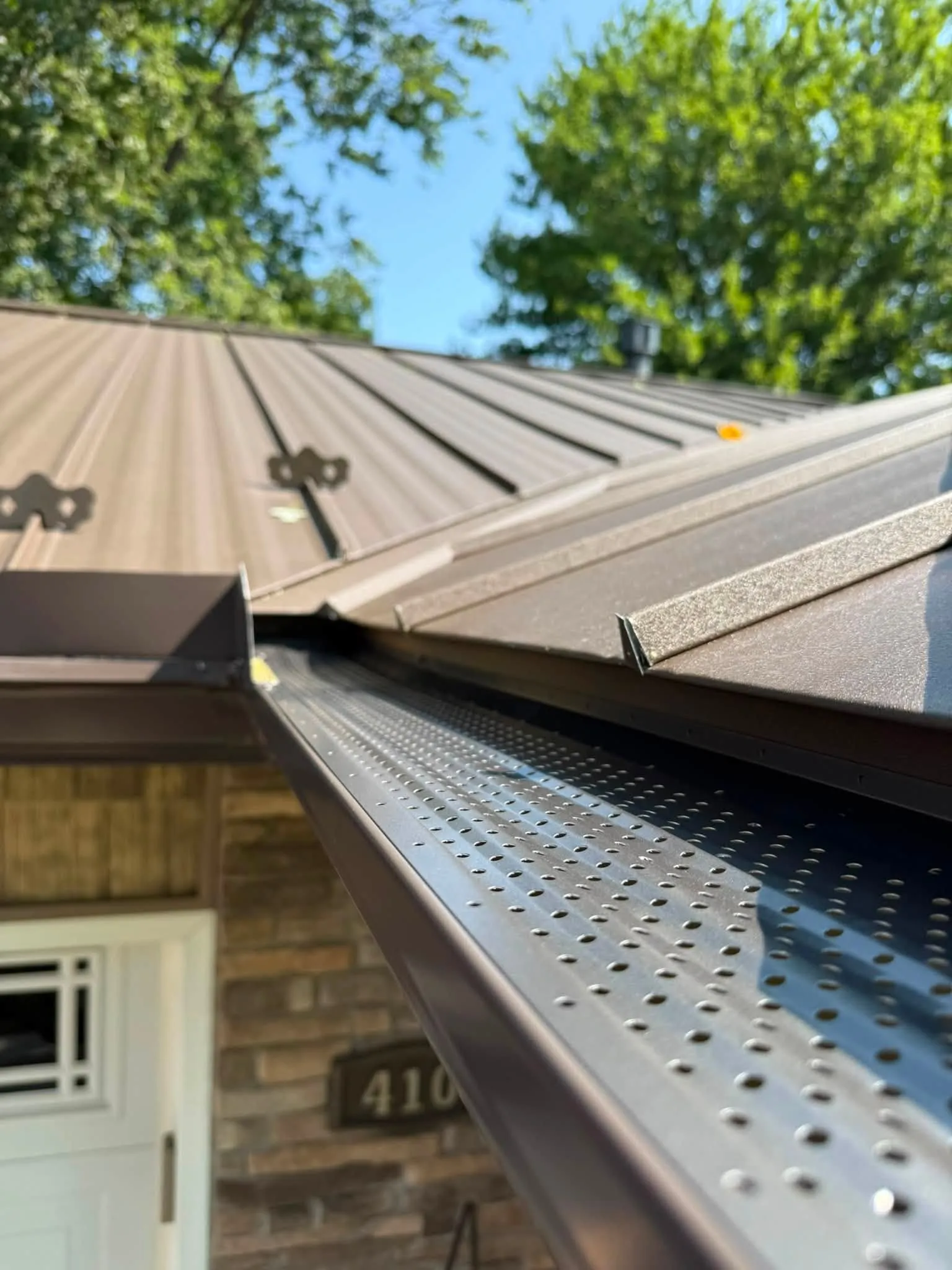 Close view of the perforated leaf guard fitted over the new gutter, with the metal roof above