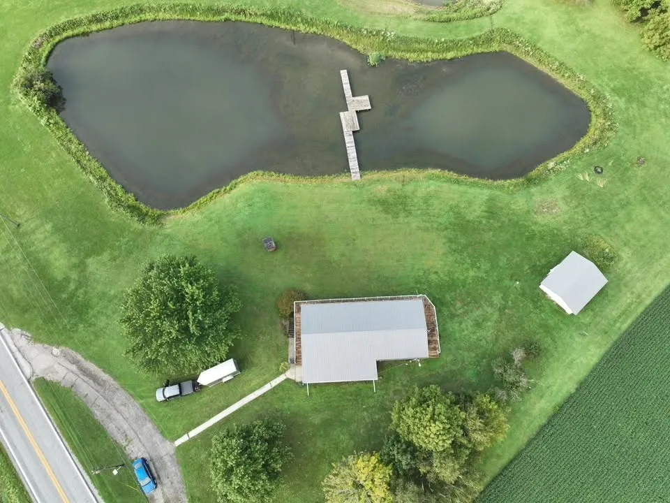 High overhead view of the property, with the house, the pond and dock, and the road alongside