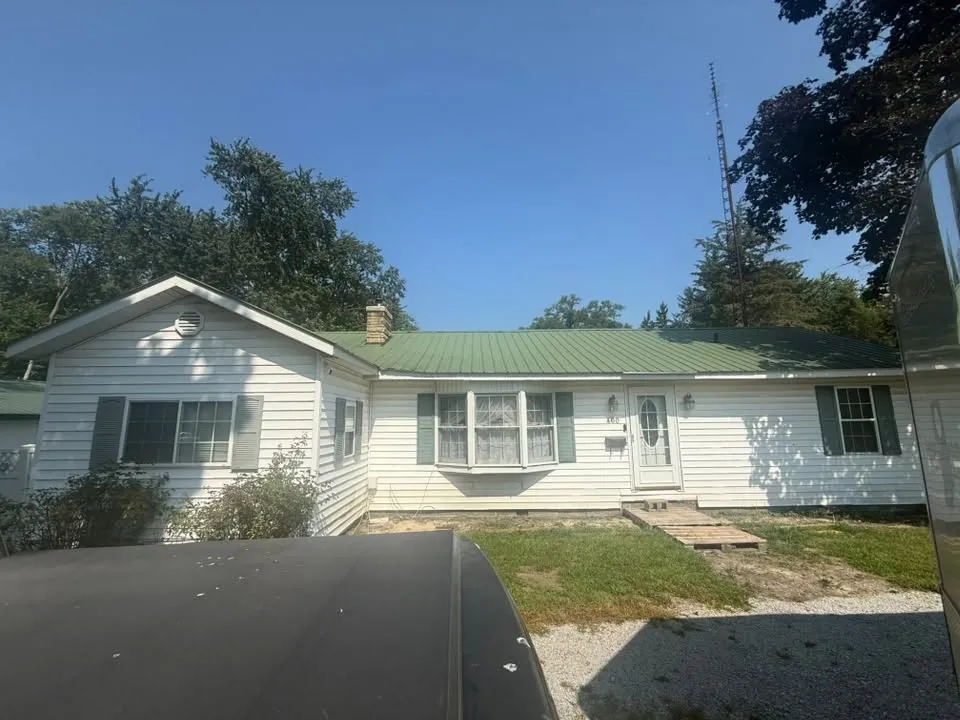 The house before the work, under its old green metal roof, with no porch across the front
