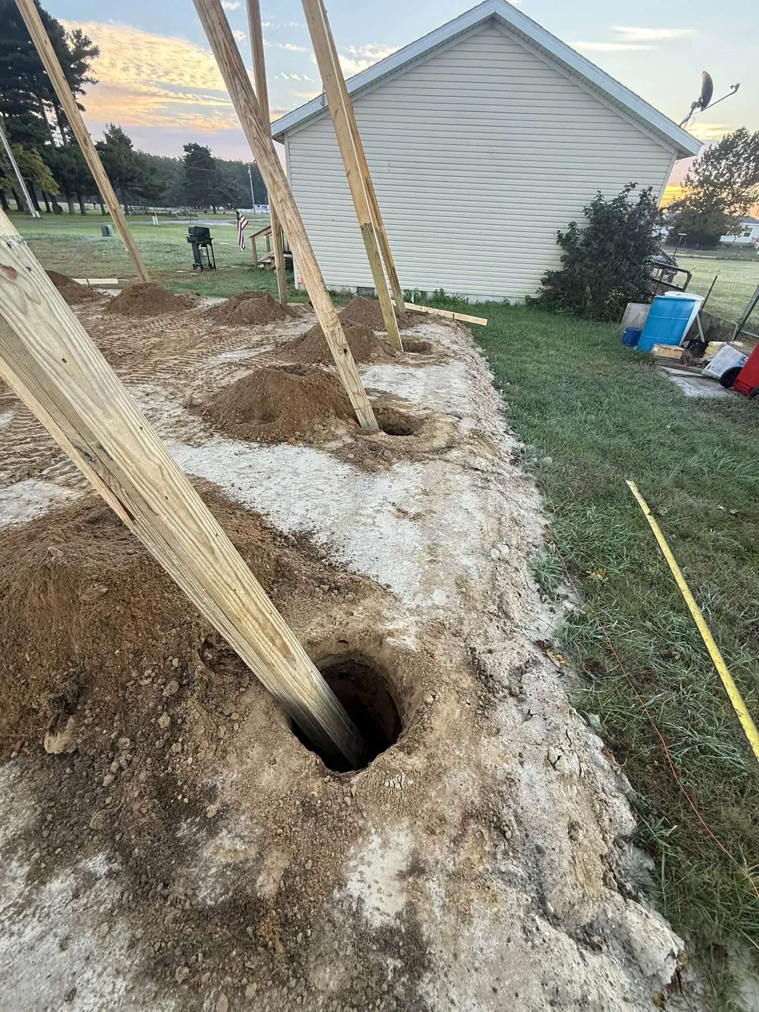 Close view of the posts standing in their augered holes, with the dug soil piled beside each one
