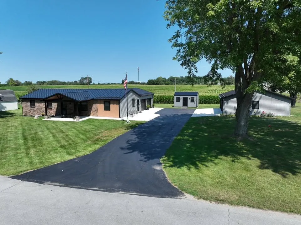 The house and its detached garage from the end of the long paved driveway, under a large shade tree