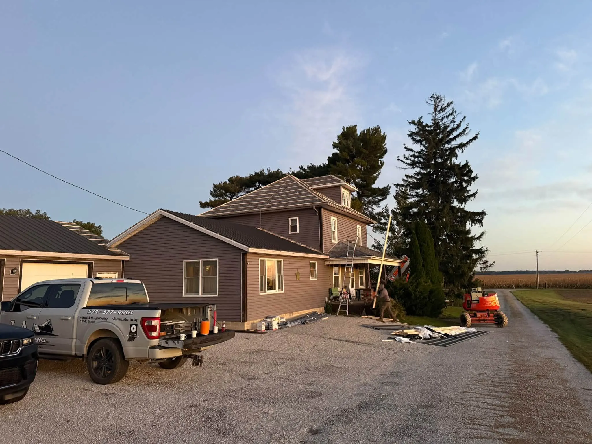 The farmhouse at dusk before the work, under its old brown roof, with the crew's truck in the drive