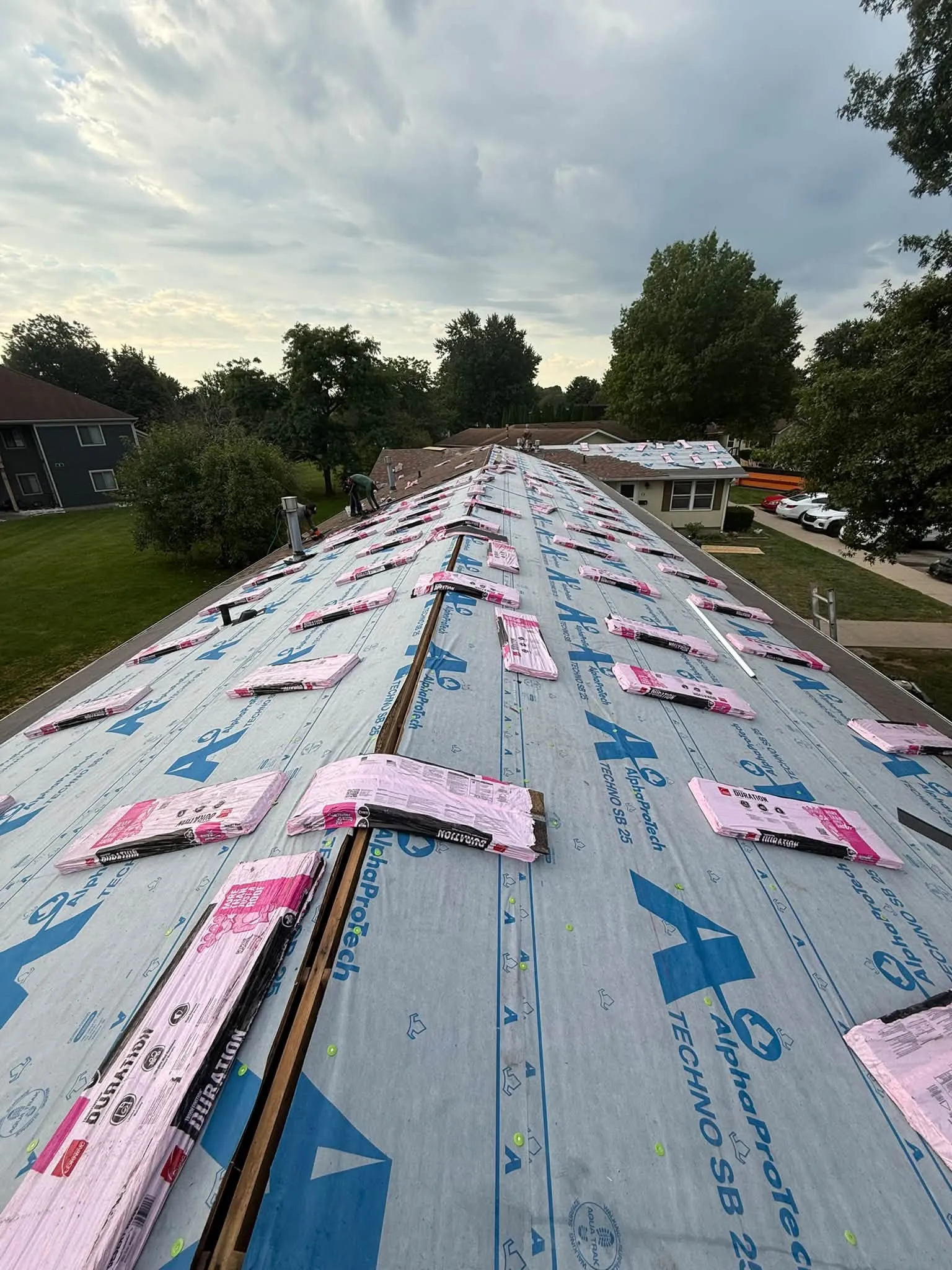 Synthetic underlayment down across a roof, with bundles of new shingles set out along the ridge