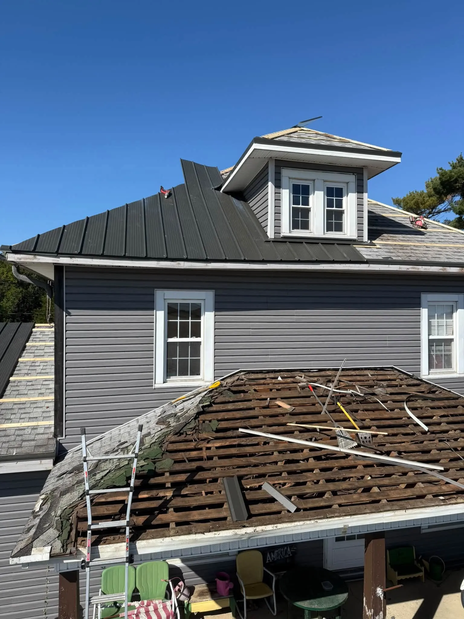 New metal panels on the upper roof and dormer, with the lower roof below still torn back to the old boards
