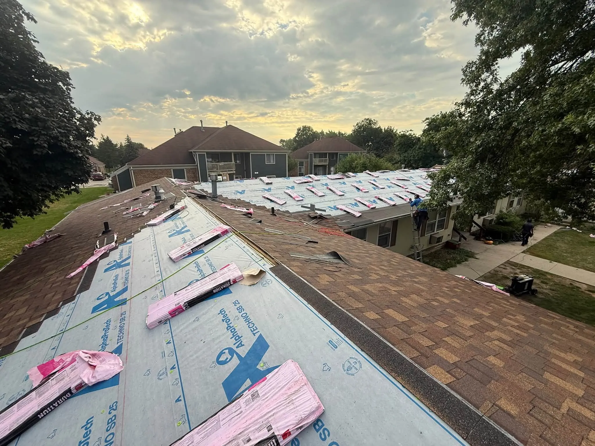 Underlayment on one slope and the old shingles still on the other, with bundles staged along the peak