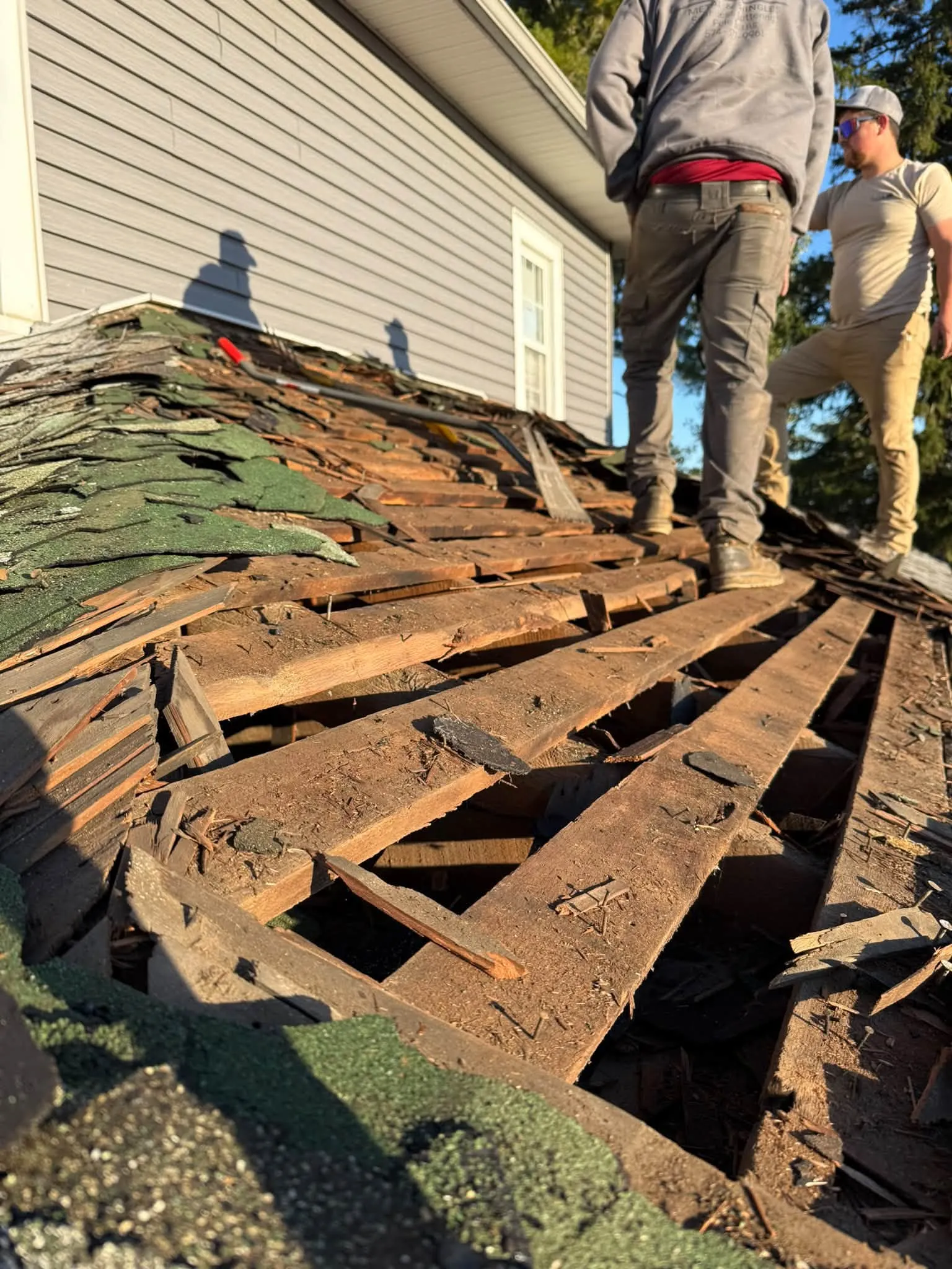 The tear-off up close, with the old roofing broken up over the spaced wood boards underneath and the crew standing on it