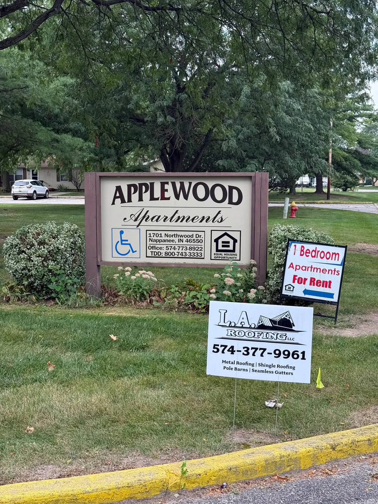 The Applewood Apartments sign by the road, with an L.A. Roofing yard sign in front of it