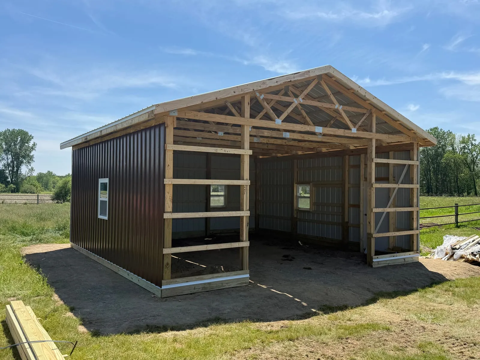 A pole barn under construction, its timber frame partially clad in dark metal siding