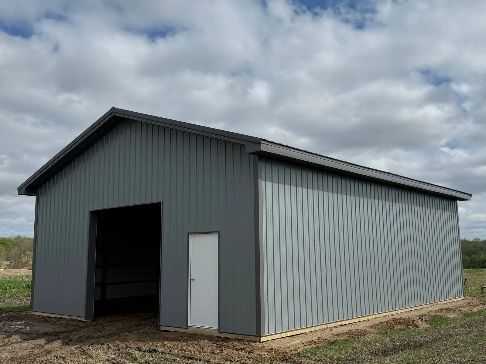 A finished grey metal pole barn with an open equipment bay, on a gravel lot