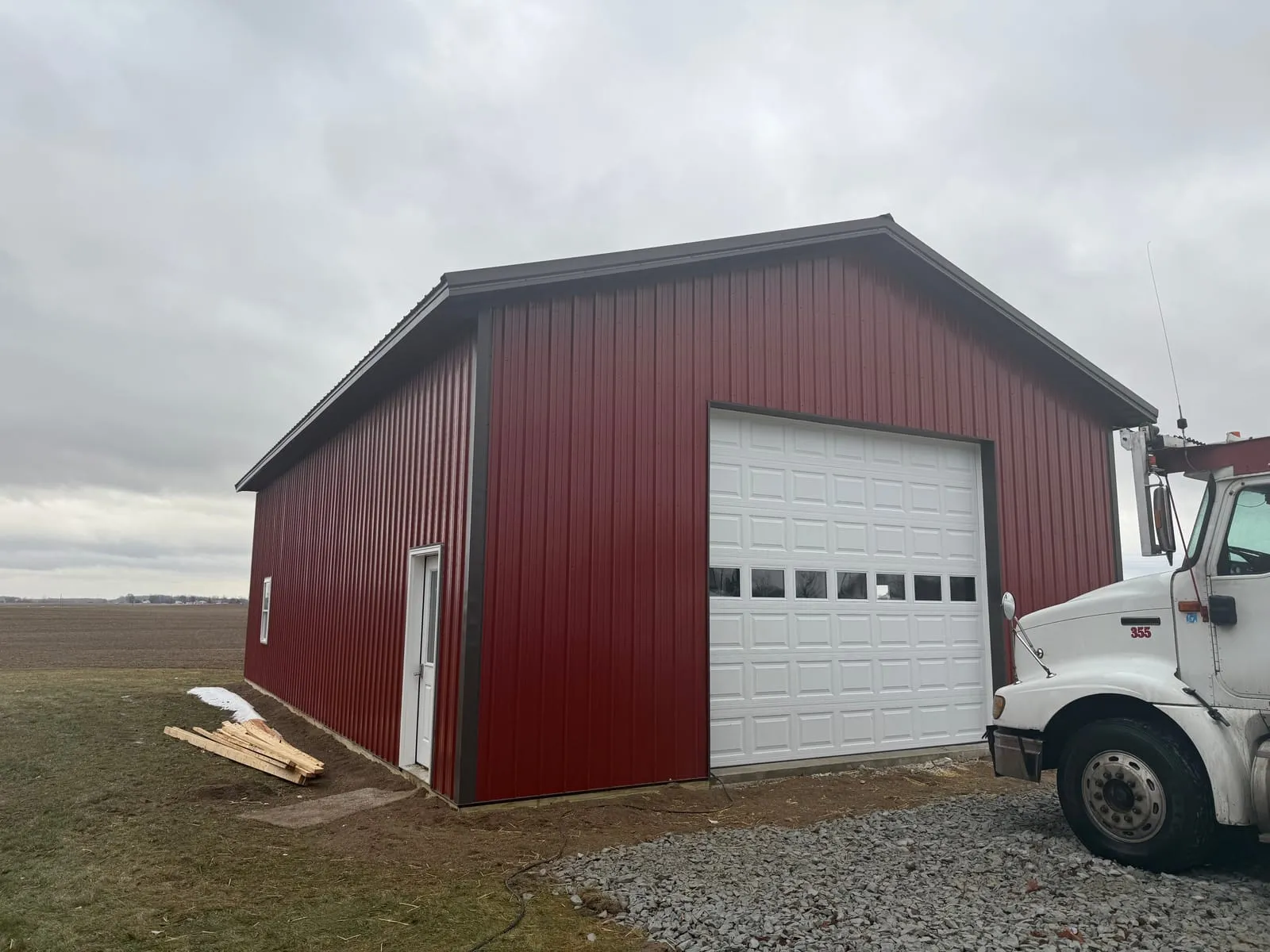 A red metal pole building with a tall white overhead door and a truck parked alongside