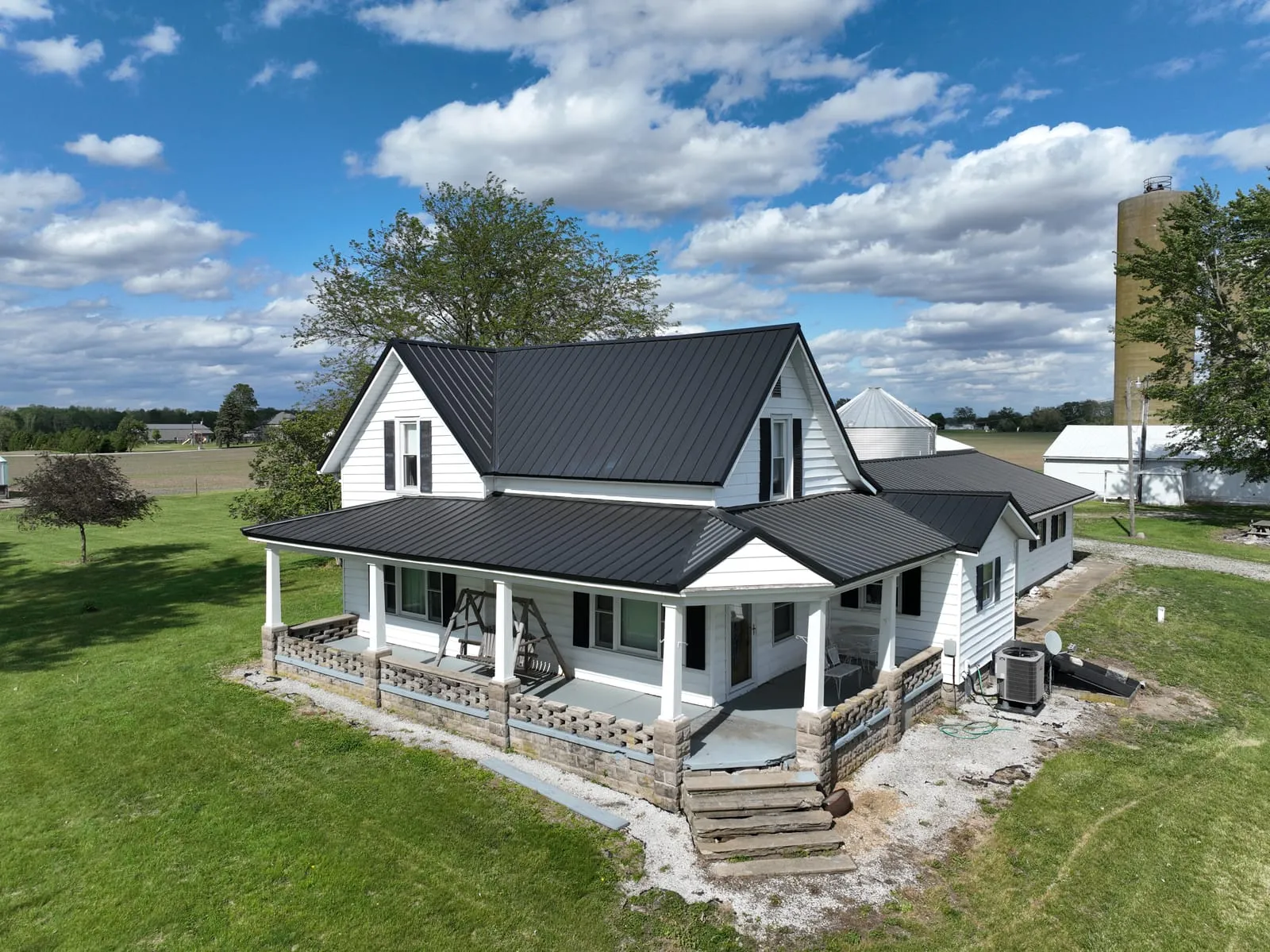 White two-story farmhouse with a charcoal metal roof and wraparound porch